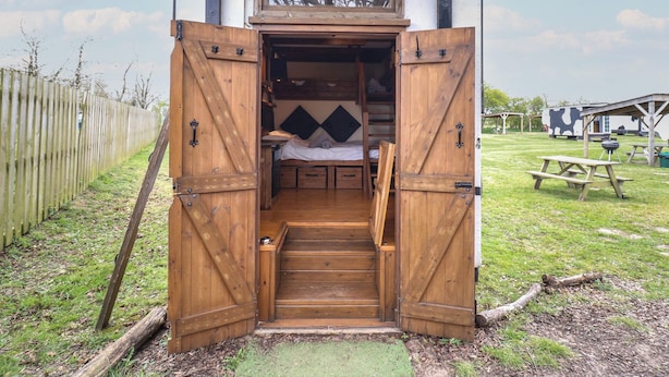 A rustic wooden cabin with a loft bed and a small entrance. - Daisy (Woodbridge)
