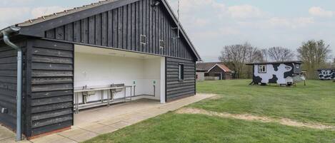 A rustic barn-style building with a covered outdoor seating area and a small cow-themed playhouse in the background.