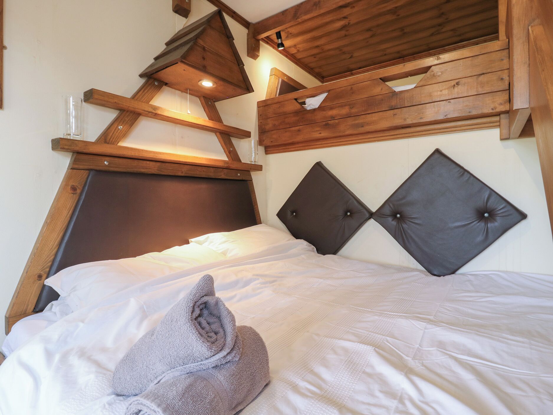 A bed with a wooden headboard, a grey towel, and a wooden ceiling structure.