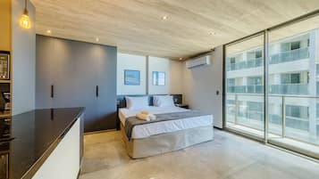 A modern bedroom with a large bed, a built-in desk, and a large window offering a view of the city.