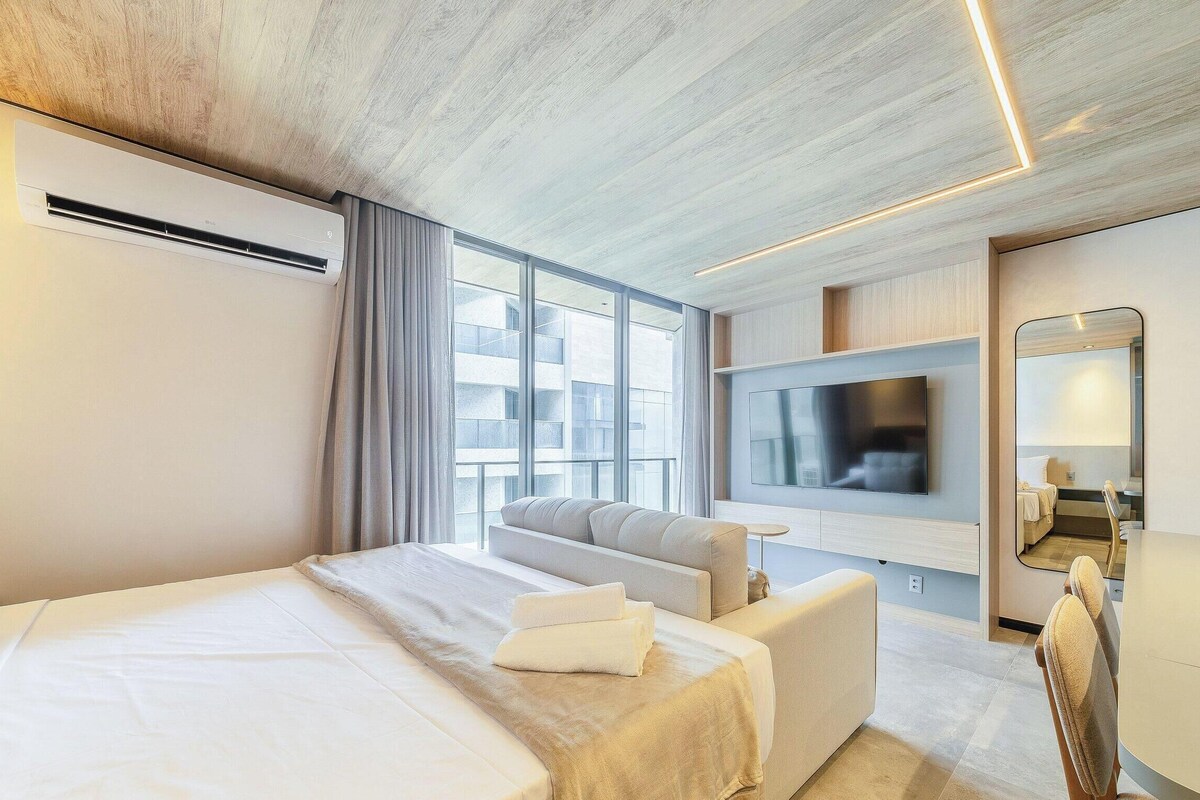 Een moderne hotelkamer met een groot bed, een bank, een flatscreen televisie aan de muur en een groot raam met uitzicht op de stad.