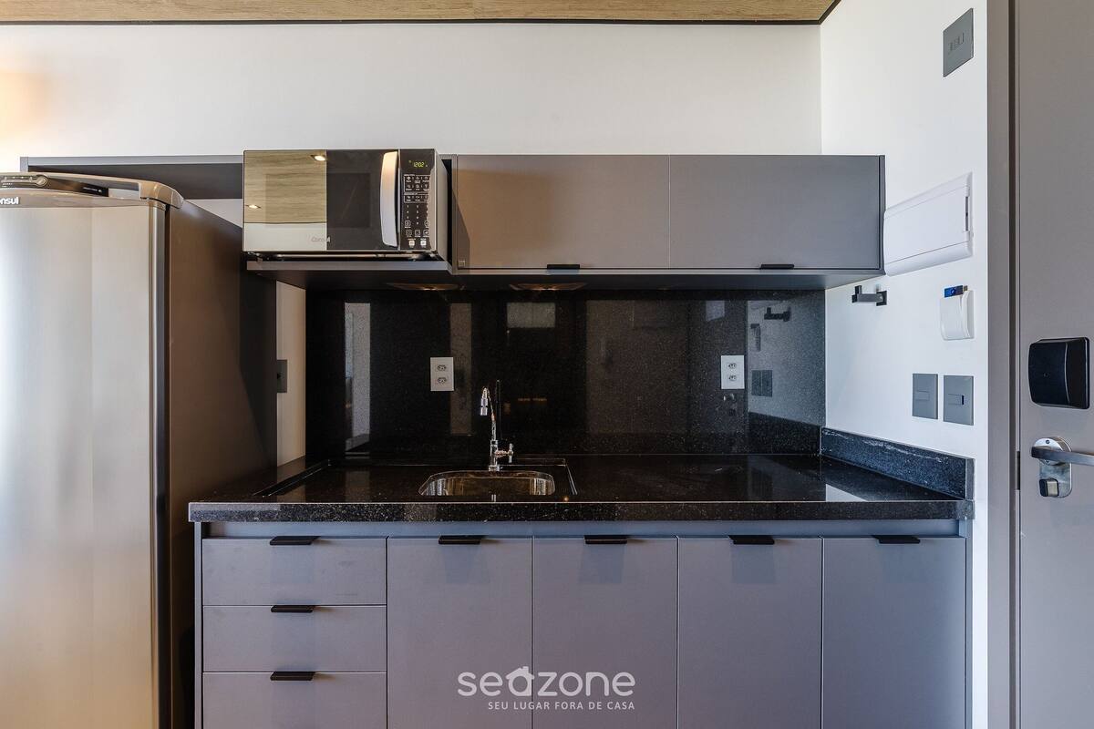 A compact kitchen with a refrigerator, microwave, and sink.