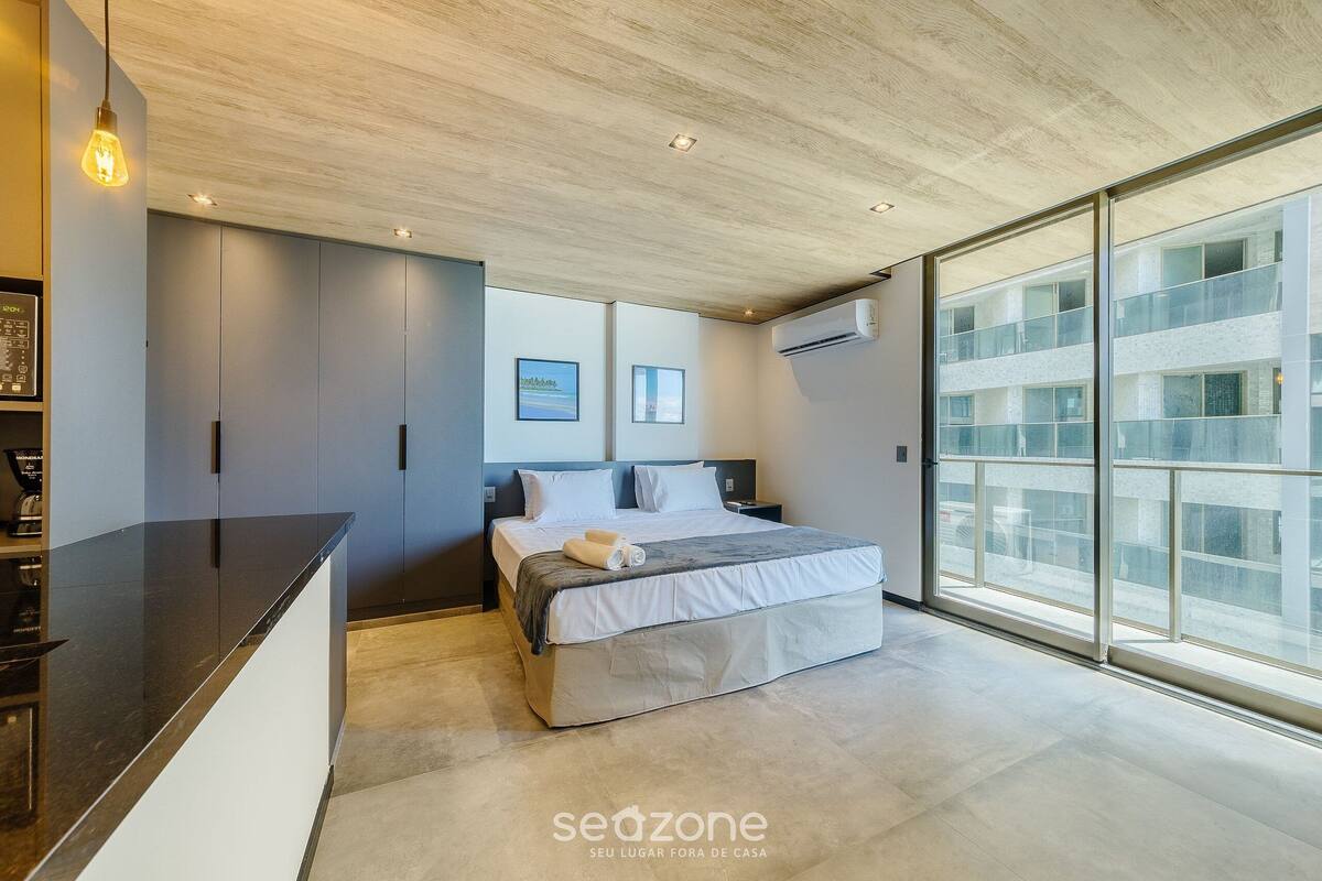 A modern bedroom with a large bed, a built-in desk, and a large window offering a view of the city.