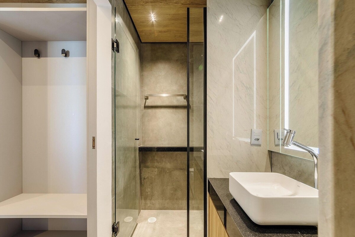 Een moderne badkamer met een douchecabine van glas, een witte wastafel en een houten plafond.