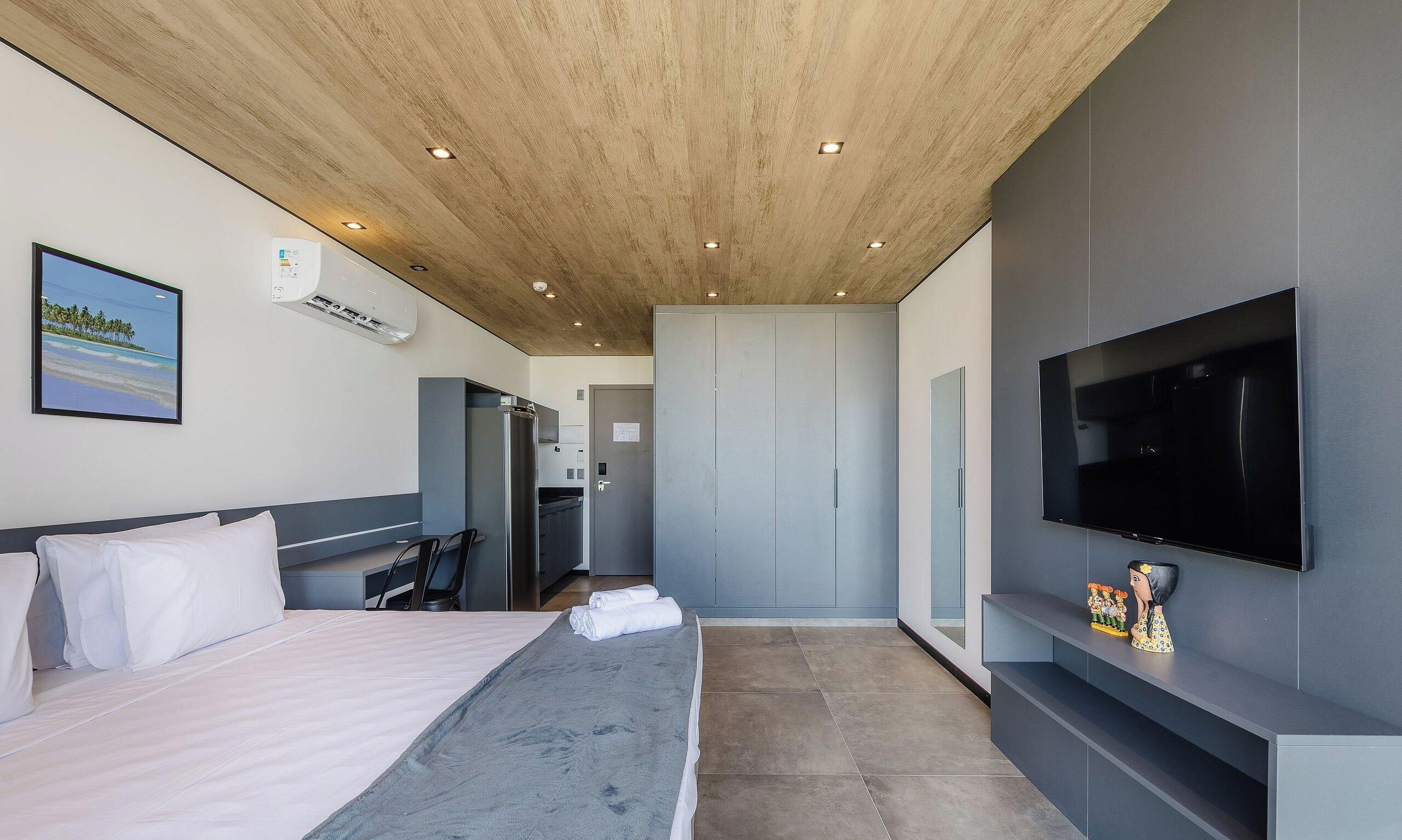 Una habitación de hotel con cama, televisión, televisor de pantalla plana en la pared, un cuadro e iluminación empotrada en el techo.