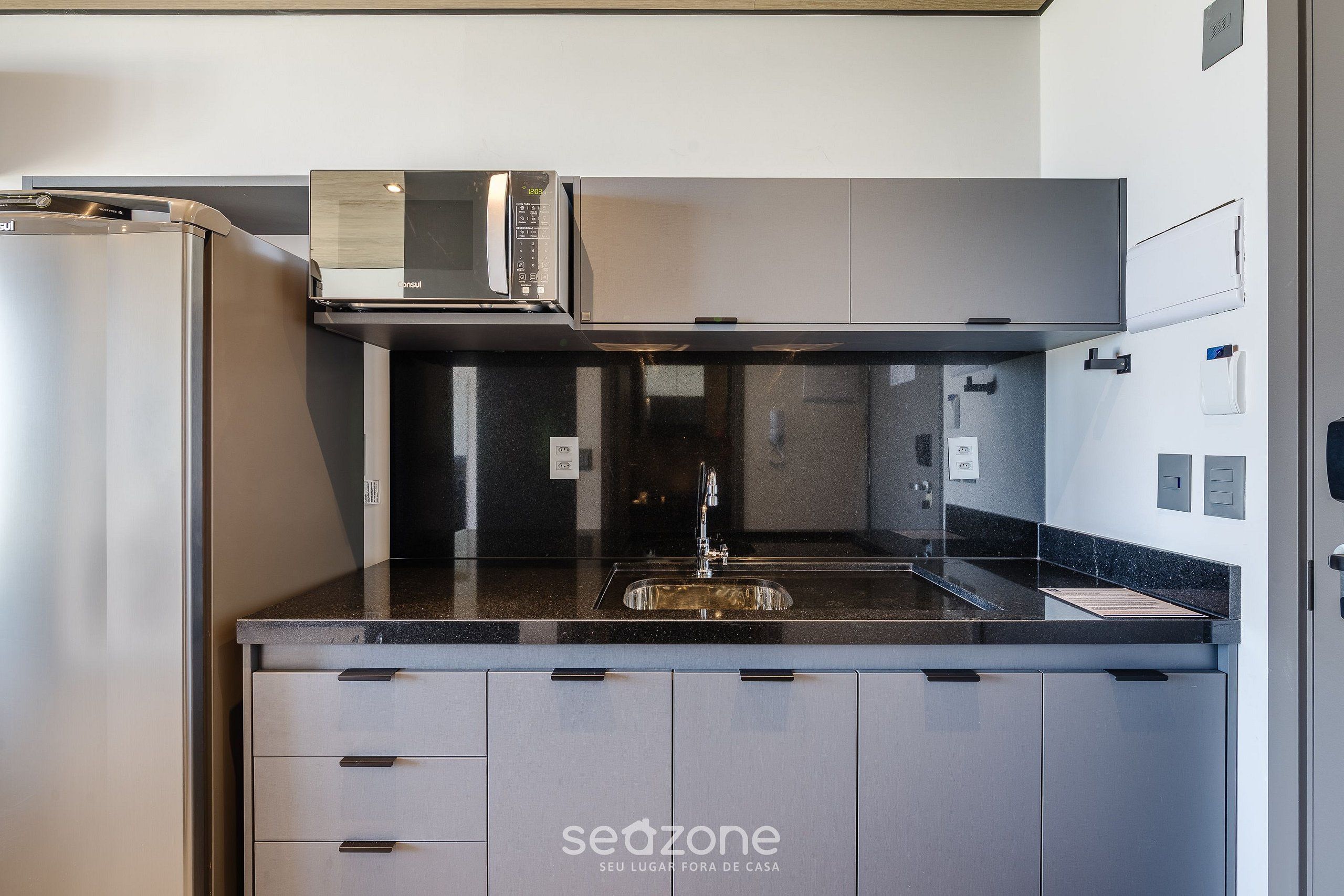 A modern kitchen with a stainless steel refrigerator, a microwave, and a sink with a black countertop.