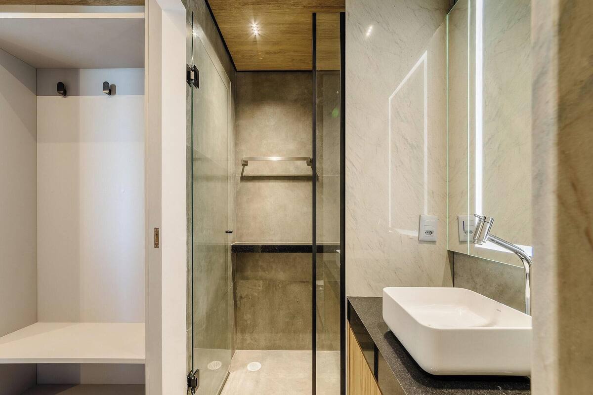A modern bathroom with a glass shower enclosure, a white sink, and a wooden ceiling.