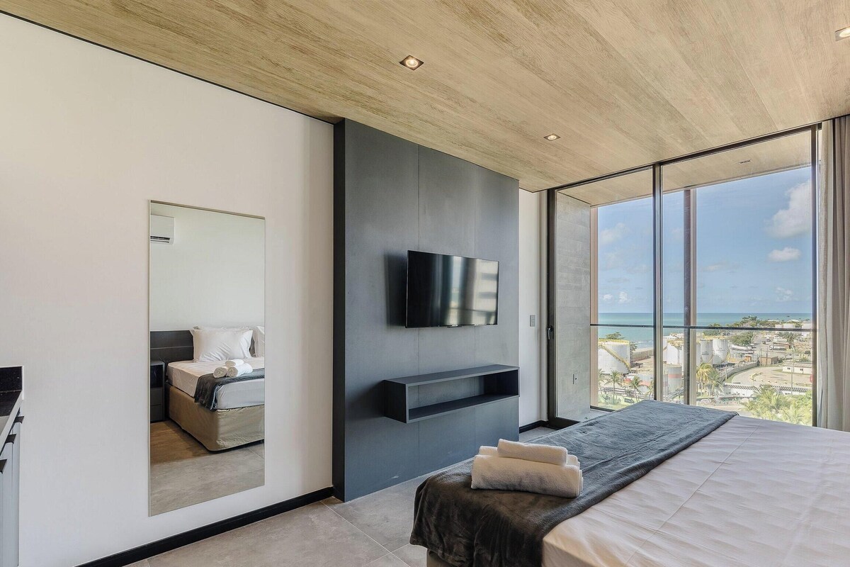 Een moderne slaapkamer met een groot bed, een flatscreen televisie aan de muur en een balkon met uitzicht over de stad.