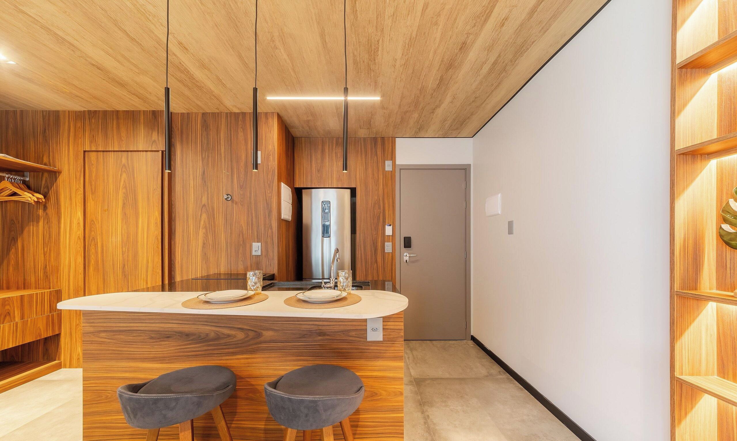 A modern kitchen with wooden cabinetry, a stainless steel refrigerator, and a central island with stools.