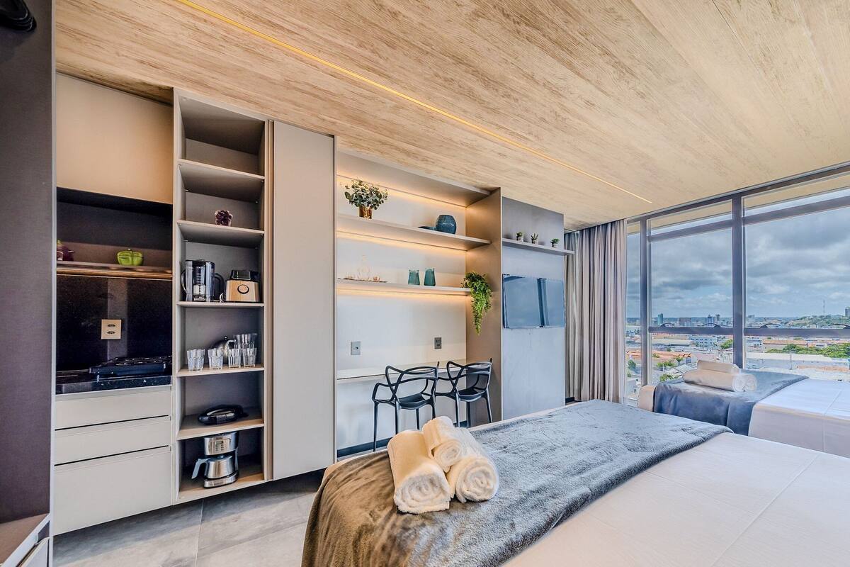 A modern bedroom with a large window, a bed, a desk, and built-in storage.