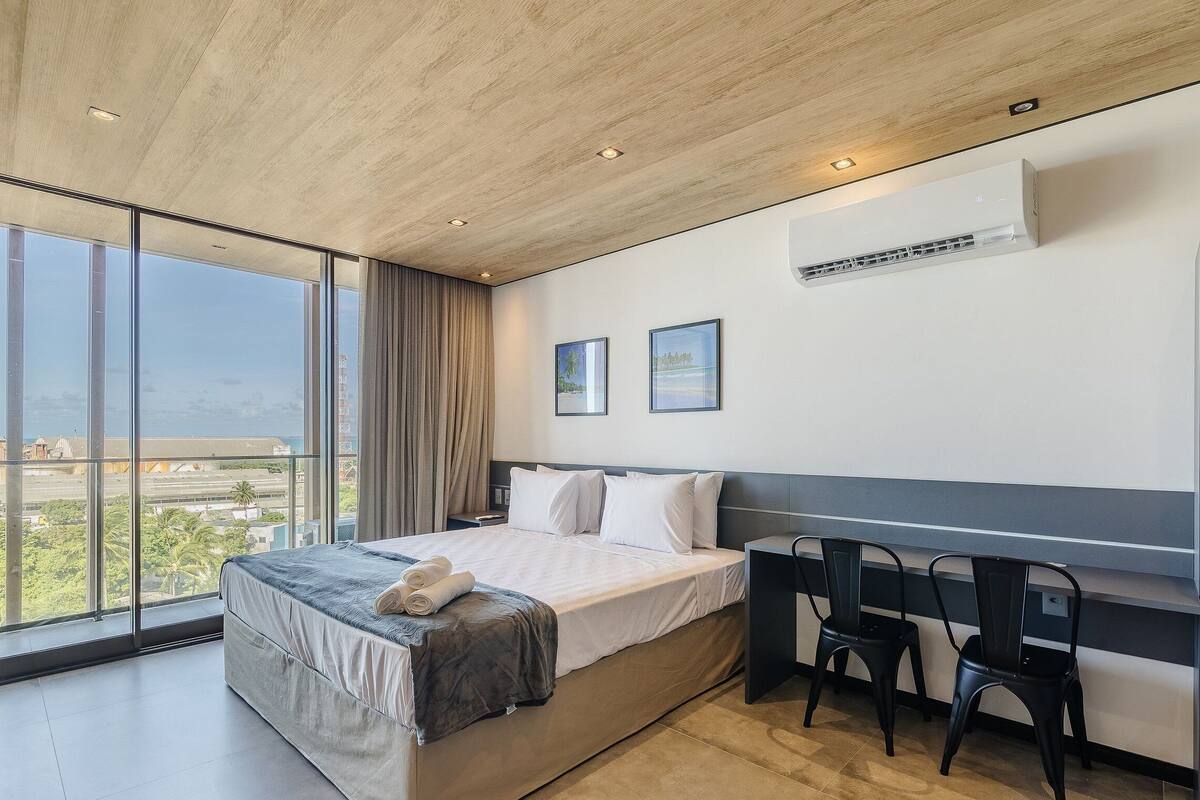 A modern hotel room with a large bed, a desk, two chairs, and a view of the city.