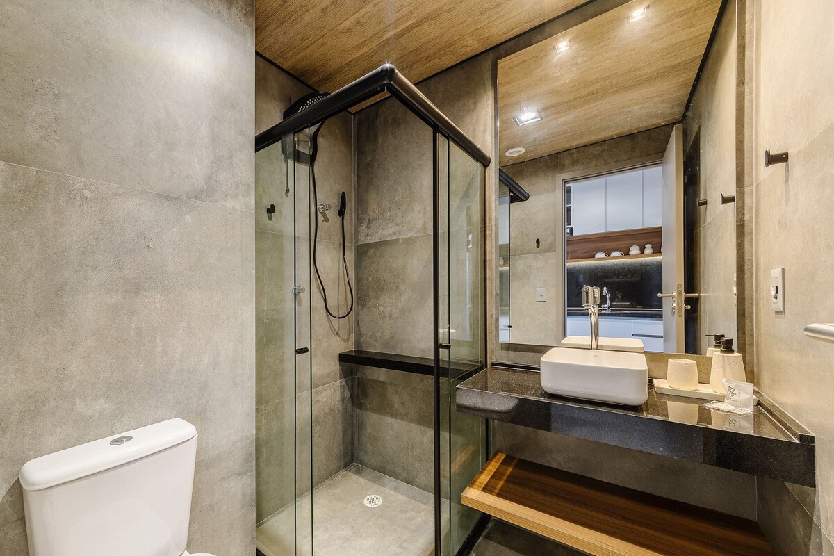 A modern bathroom with a glass-enclosed shower, a white toilet, and a black countertop with a sink and toiletries.