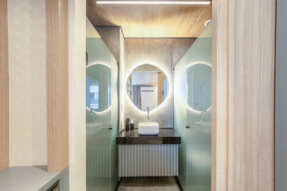 A modern bathroom with a central sink, two mirrors, and a ceiling light.