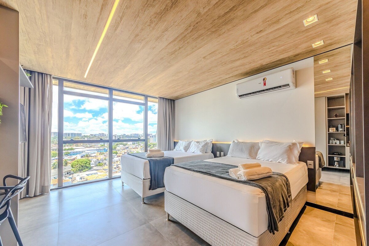 Een moderne hotelkamer met een groot bed, een bureau en een stadszicht door grote ramen.