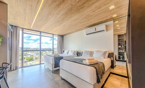 Een moderne hotelkamer met een groot bed, een bureau en een stadszicht door grote ramen.
