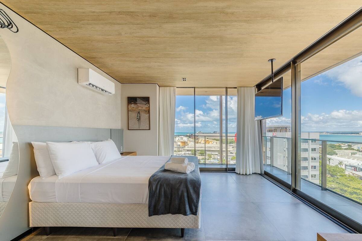 A modern hotel room with a large bed, a view of the city, and a balcony.
