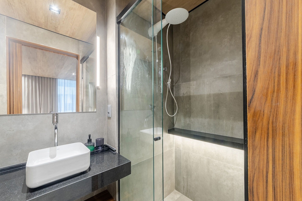 Een moderne badkamer met een douchecabine van glas, een witte wastafel en een houten opbergmeubel.