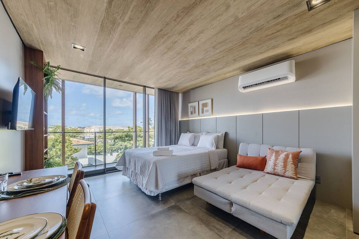 A modern hotel room with a large bed, a sofa, a dining area, and a view of the city.