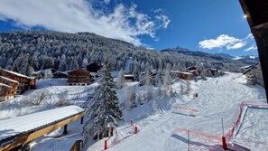 A snow-covered ski resort with wooden buildings, a ski slope, and a forested mountain backdrop.