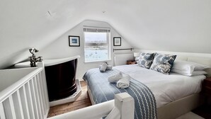 A bedroom with a large bed, a window with a view of the sea, a fireplace, and a small table with a lamp. - Sleeps 6 guests  in 3 bedrooms (St Ives, Saint Ives)