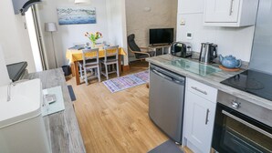 A compact kitchen with a dishwasher, a stove, a sink, and a small dining area with a table and chairs. - 3 The Barn (Haverfordwest)