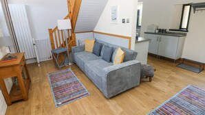 A cozy living room with a sofa, a wooden table, a lamp, and a kitchen area in the background. - 3 The Barn (Haverfordwest)