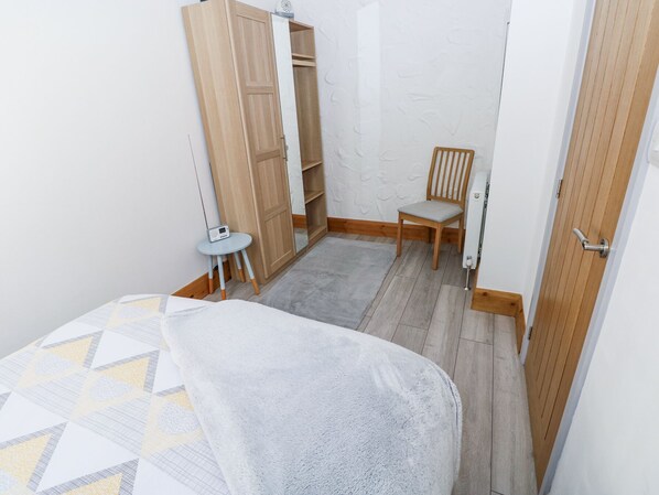 A small room with a bed, a wooden wardrobe, a chair, and a small table with a radio. - 3 The Barn (Haverfordwest)