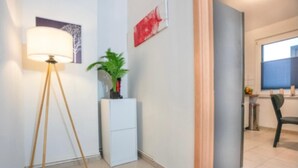 A room with a floor lamp, a small plant, a white cabinet, a black rug, and a dining area with a chair.