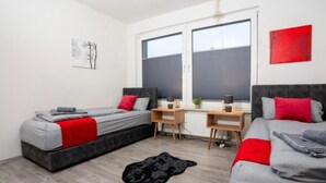 A modern bedroom with two beds, a desk, and a large window.