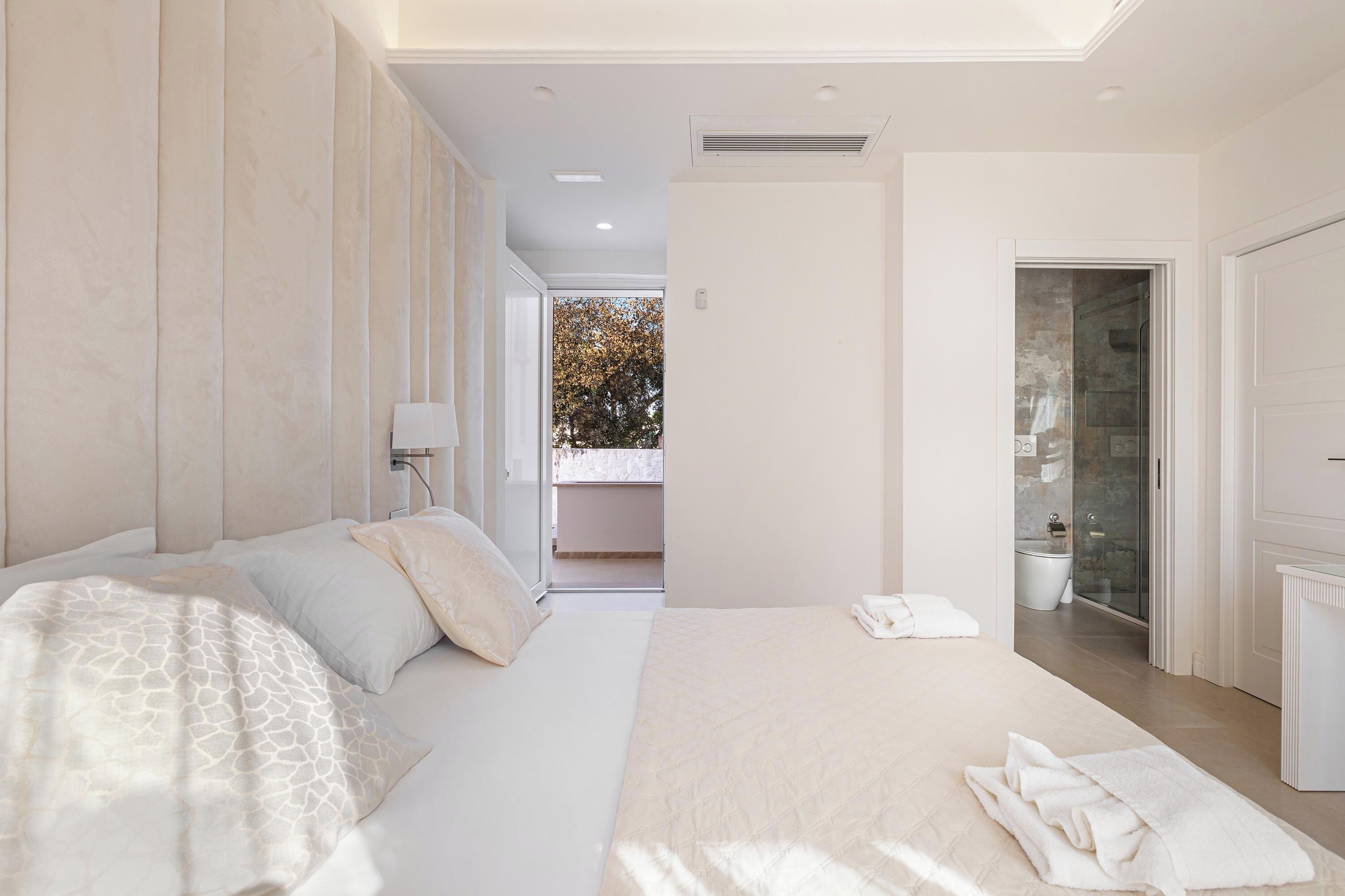 A modern bedroom with a large bed, a bedside table, and a view of a balcony.
