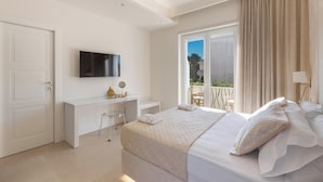 A modern hotel room with a large bed, a desk with a computer, and a balcony with a view.