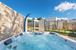 Un jacuzzi con un muro de piedra de fondo, una cerca y un cielo azul despejado.