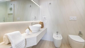 Ein modernes Badezimmer mit einem großen Spiegel, einem weißen Waschbecken, einem Bidet und einer Toilette.