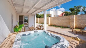 Un espacio al aire libre techado con un jacuzzi, mobiliario de madera y una pared de piedra.