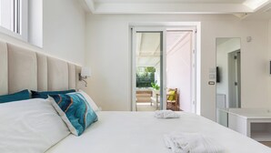Habitación de hotel con una cama grande, una mesita de noche, un espejo y una puerta que da a un espacio exterior.