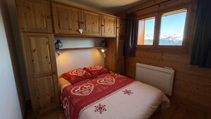 Et træhytteværelse med seng, indbyggede skabe, en radiator og et vindue med udsigt til et bjerglandskab.