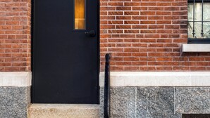 Una puerta negra con el número 829 sobre un muro de ladrillo, escalones de piedra y una barandilla metálica.