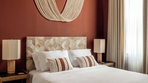 Una cama bien tendida con sábanas blancas y almohadas a rayas, un cabecero con estampado geométrico y dos lámparas de noche sobre mesitas de madera.