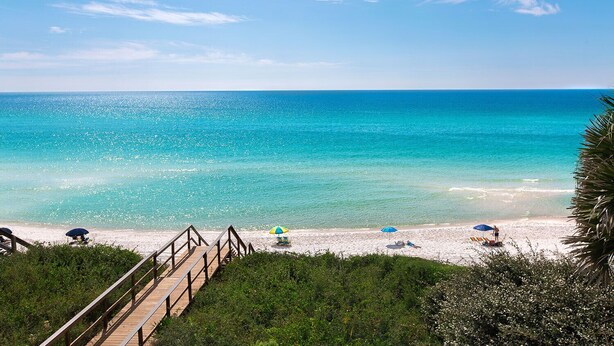 Une plage à l’eau turquoise et limpide, avec des passerelles en bois et des parasols.