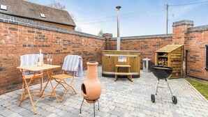 A patio with a table, chairs, a large urn, a hot tub, and a barbecue grill. - The Little House - UK49129 (Stapleton)