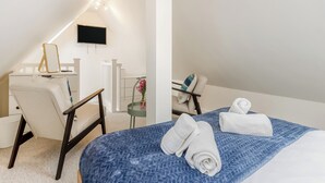 A hotel room with a bed, a desk with a chair, a TV mounted on the wall, and a small table with a vase of flowers. - The Little House - UK49129 (Stapleton)