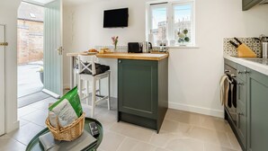 A compact kitchen with a built-in oven, a window with a view, a TV mounted above the counter, and a small dining area with a chair. - The Little House - UK49129 (Stapleton)