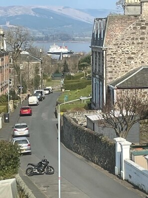 A street view with parked cars, a motorcycle, and a boat in the background. - Isle of Bute Blissful Retreat- Stunning 3 Bed Flat (Rothesay)
