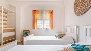 Un dormitorio con dos camas, un armario y una ventana con cortinas naranjas.