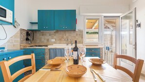 Una mesa de comedor con platos, copas de vino y cubiertos en una cocina con armarios azul verdoso y un salpicadero de azulejos.