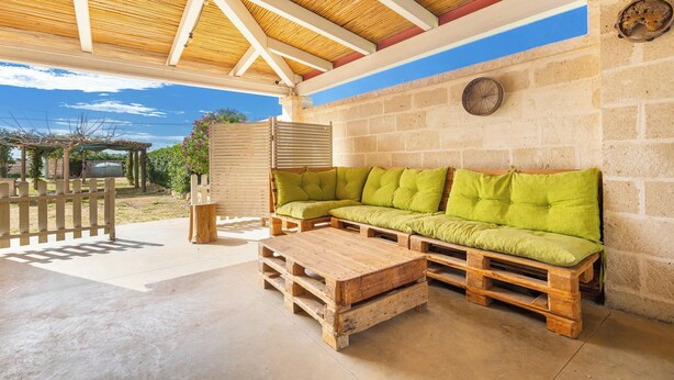 Un patio cubierto con un banco de madera y un sofá, una pared de piedra y un techo de madera.