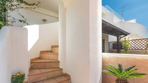 Una escalera conduce a un espacio exterior cubierto, con una planta en maceta y vistas a un edificio blanco con balcones.