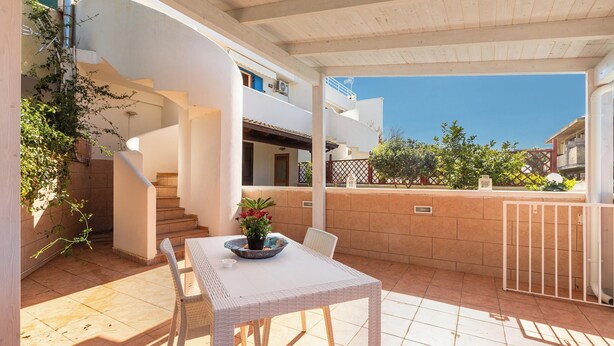 Un patio techado con una mesa y sillas, una planta en maceta y vistas de los edificios circundantes.