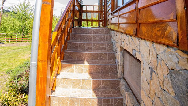 Un escalier en bois mène à une véranda aux murs en pierre, avec un ciel dégagé en arrière-plan.