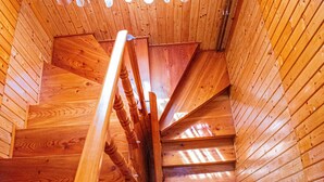 Un escalier en colimaçon en bois, doté d’une rampe métallique, se trouve à l’intérieur d’une cabane aux murs en bois et au plafond incliné.